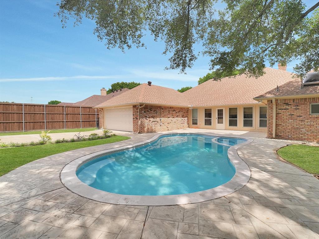 Outdoor oasis featuring a freeform swimming pool, stamped concrete decking, and a brick-clad exterior