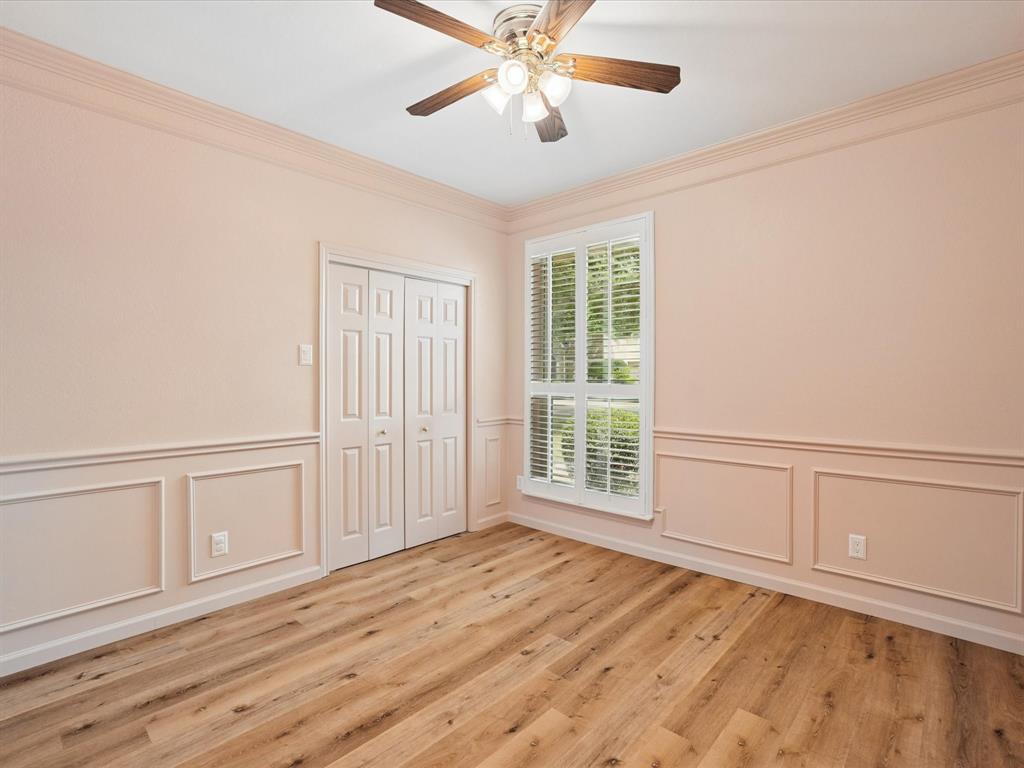 Wood-finish flooring, crown molding, wainscoting, bi-fold closet doors, and a ceiling fan with light fixture