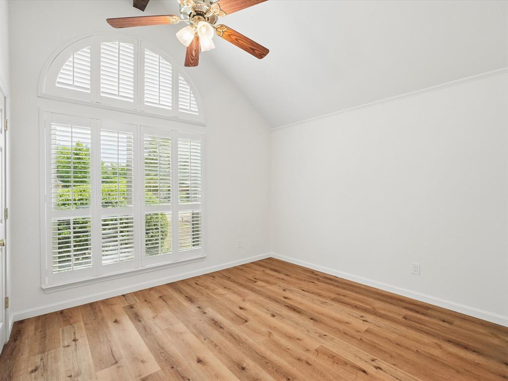 Wood-finish flooring, vaulted ceiling, arched window, white plantation shutters, and ceiling fan with lighting fixture
