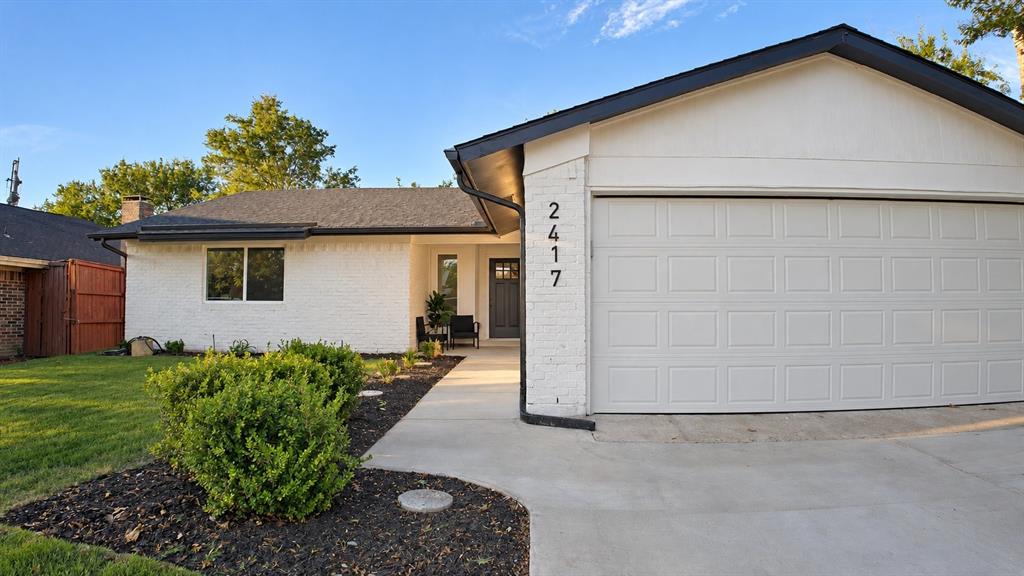 White brick exterior with black trim, a paneled garage door, a concrete driveway, and a front walkway