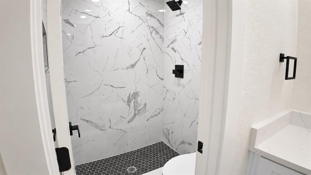 Walk-in shower with black hexagonal tile flooring and white marble-look wall tiles