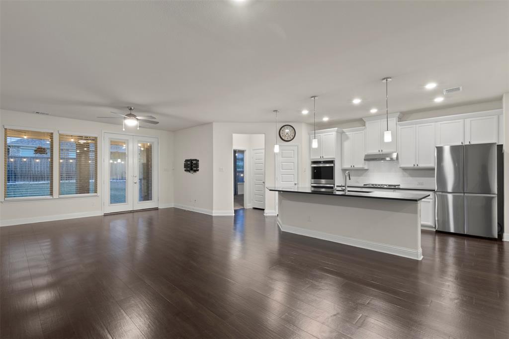 Hardwood-finish flooring, white cabinetry, stainless steel appliances, kitchen island with dark countertop, and recessed lighting