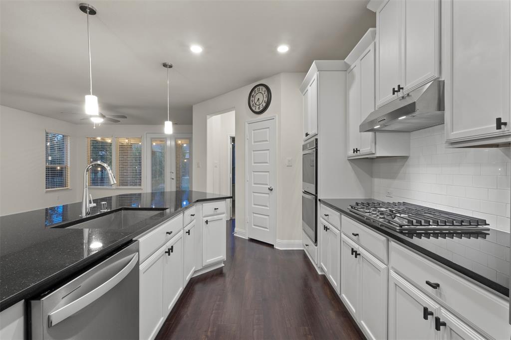 White cabinetry with dark hardware, dark stone countertops, stainless steel appliances, and wood-finish flooring