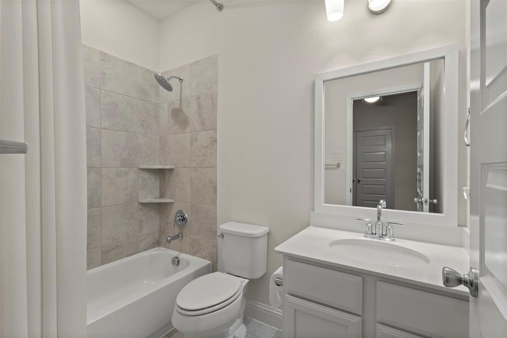 Full bathroom featuring a white vanity with an integrated sink, a framed mirror, and a tub with tiled surround and built-in shelving