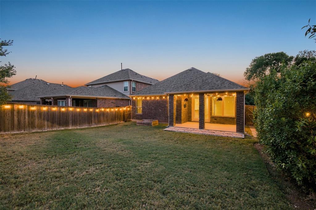 Expansive backyard featuring a covered patio with brick columns, string lighting, and a wood privacy fence