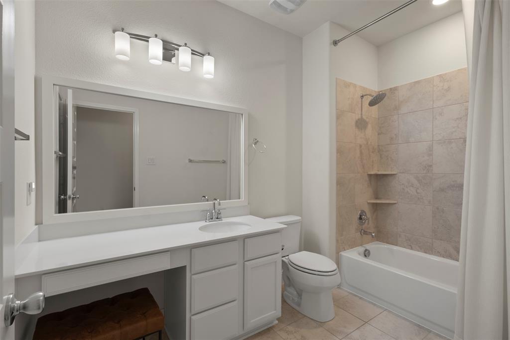 White vanity with integrated sink, expansive framed mirror, contemporary four-light fixture, tub with tiled surround, and built-in shower shelving