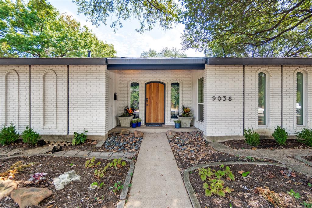 White brick exterior with a flat roofline, featuring an arched wooden entry door