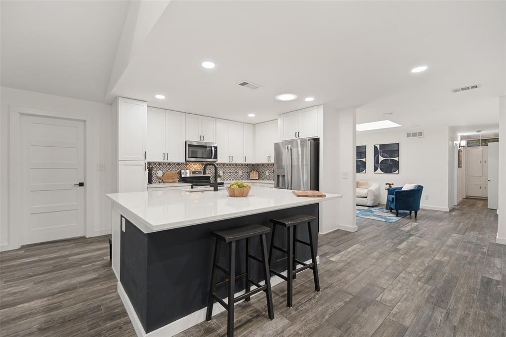 Kitchen featuring a central island with countertop seating, white cabinetry, integrated stainless steel appliances, and wood-finish flooring