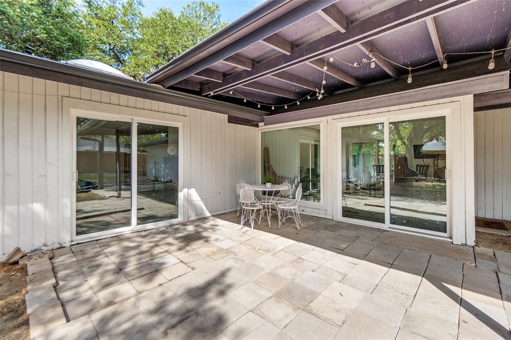 Paved patio with multiple sliding glass doors, a wood-beam overhang, and plank siding