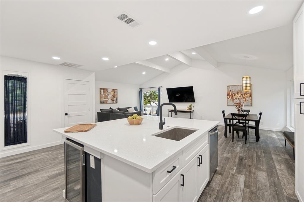 Open-concept living space with vaulted ceilings, wood-finish flooring, a kitchen island featuring a built-in beverage cooler, and recessed lighting