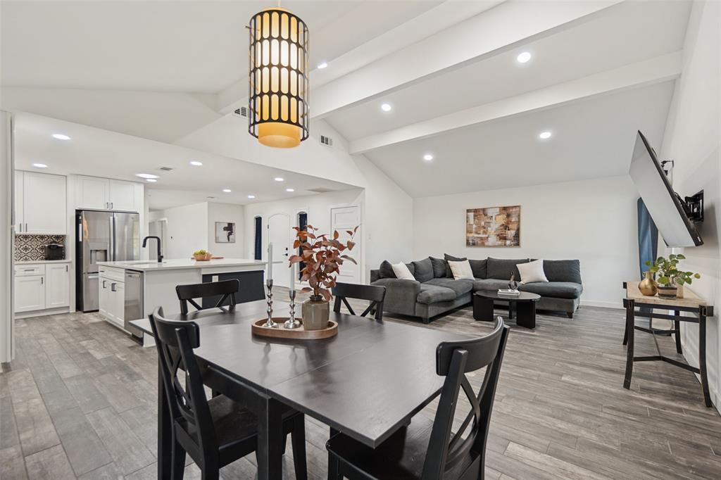 Vaulted ceilings with exposed beams, wood-finish flooring, recessed lighting, and a modern kitchen island with an undermount sink