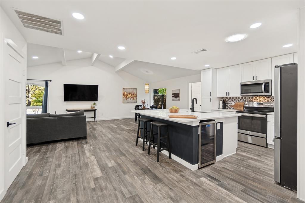 Vaulted ceilings, wood-finish flooring, white cabinetry, stainless steel appliances, and a kitchen island with built-in beverage refrigerator