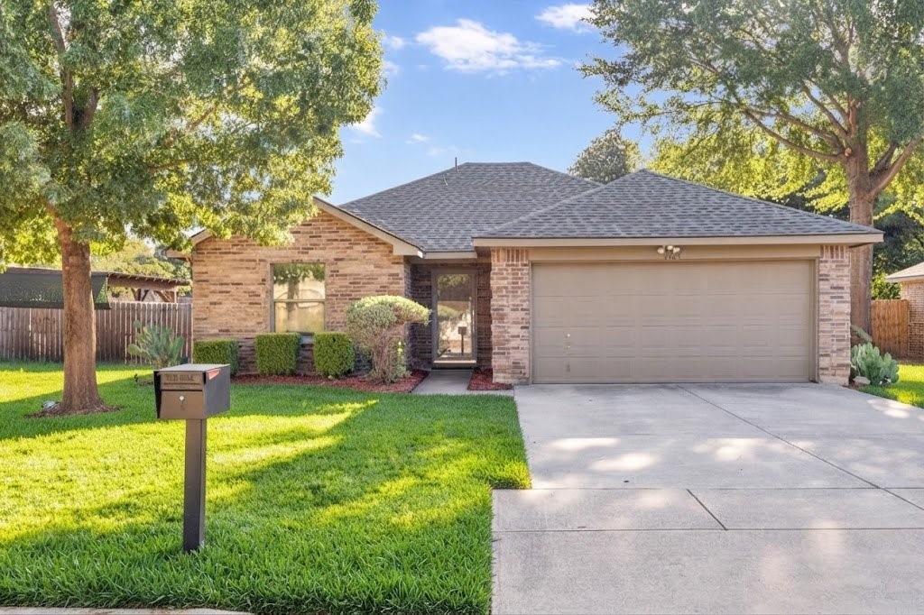Brick facade with stone accents, a concrete driveway, an attached garage, and mature trees