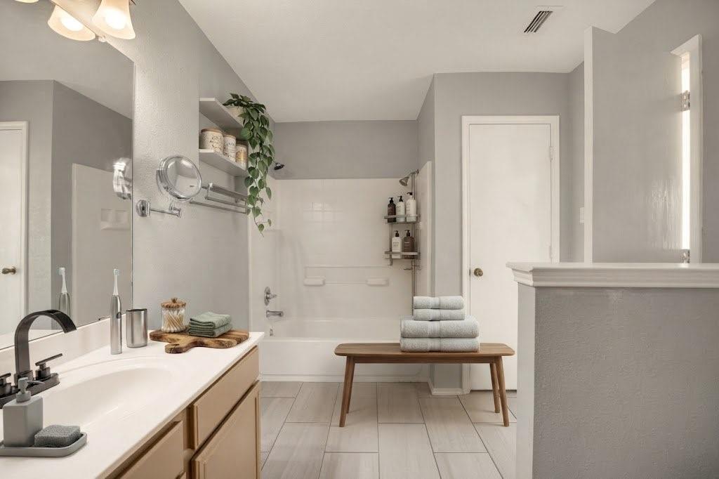 Bathroom featuring a single vanity with a white countertop and matte black faucet, a bathtub with a shower, and tile flooring