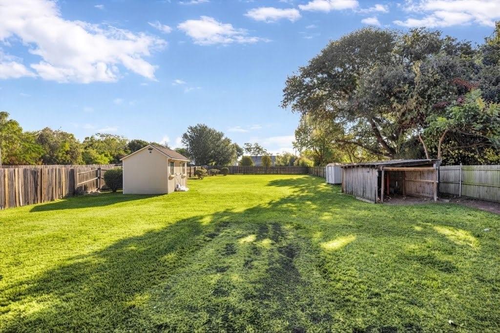 Expansive lawn featuring perimeter fencing, a freestanding shed, and mature trees