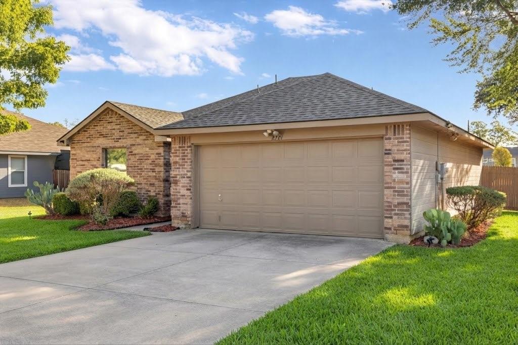 Brick exterior with an attached garage, concrete driveway, and manicured landscaping