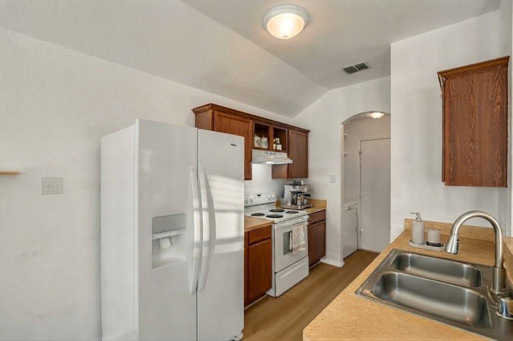 Kitchen featuring wood-finish cabinetry, a double basin stainless steel sink, a range with an overhead exhaust, and a side-by-side refrigerator