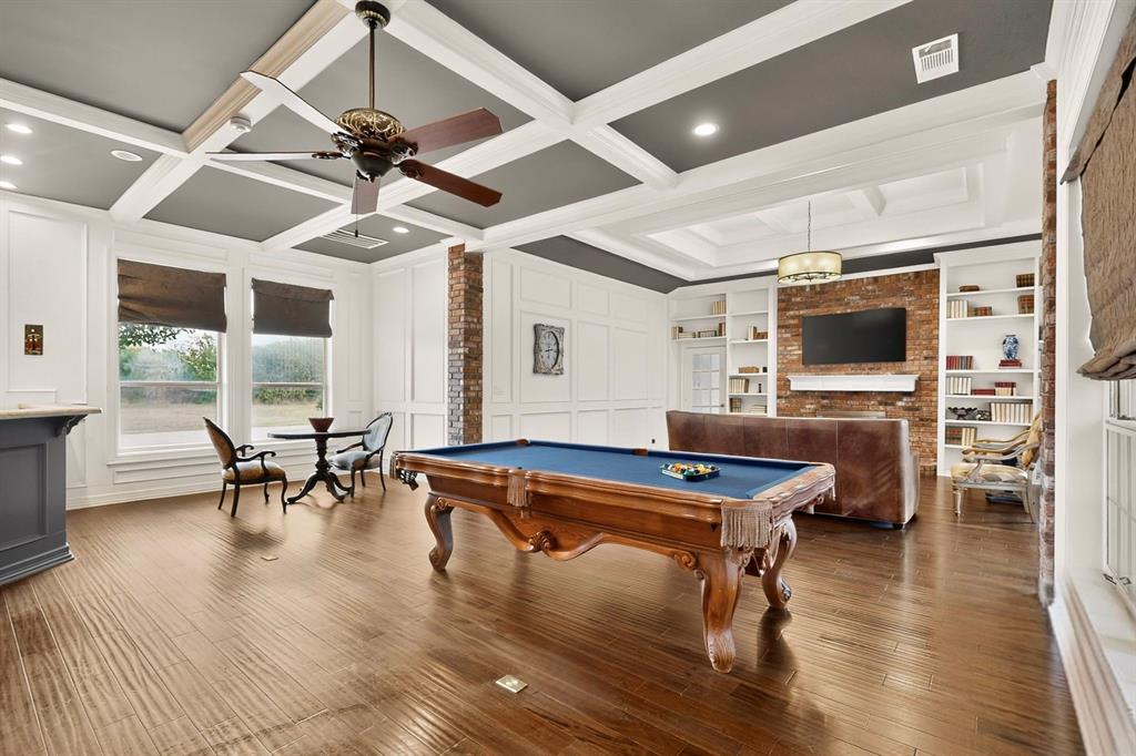 Coffered ceiling with contrasting paint, exposed brick fireplace, built-in cabinetry, wood-finish flooring, and crown molding