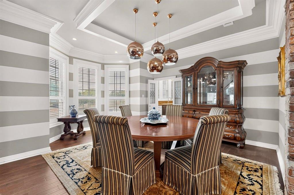 Dining area featuring a recessed tray ceiling, multi-light metallic pendant fixture, bay window configuration, and wood-finish flooring