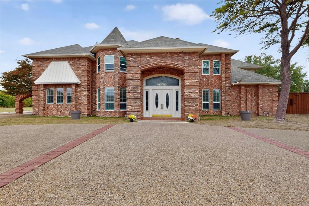 Multi-story brick exterior featuring a prominent turret, arched entryway, double front doors with leaded glass accents, and a custom-patterned concrete driveway