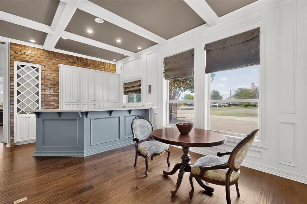 Coffered ceiling, exposed brick wall, custom built-in wine rack, stone-topped island with cabinetry, and wood-finish flooring