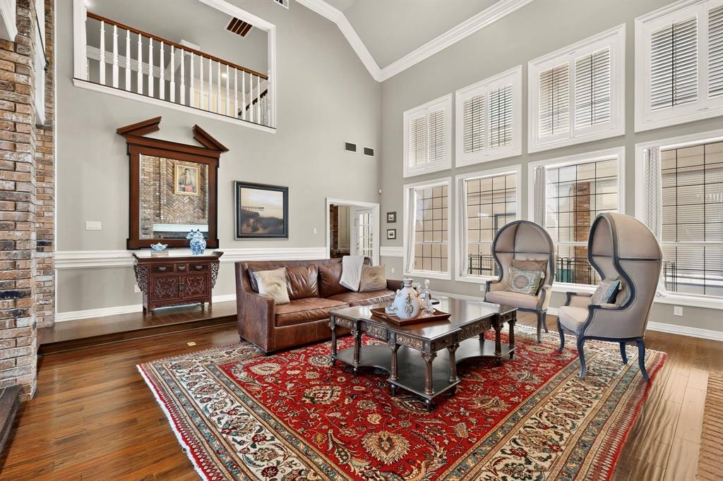 Vaulted ceiling featuring a mezzanine overlook with white railing, floor-to-ceiling windows with plantation shutters, wood-finish flooring, and a floor-to-ceiling brick fireplace surround