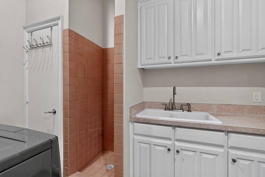 Built-in white cabinetry, drop-in utility sink with high-arc faucet, solid-surface countertop, and floor-to-ceiling square tile surround