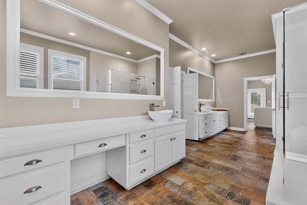 Dual vanity featuring white shaker-style cabinetry, solid-surface countertops, vessel sinks, expansive wall-mounted mirrors, and multi-toned tile flooring