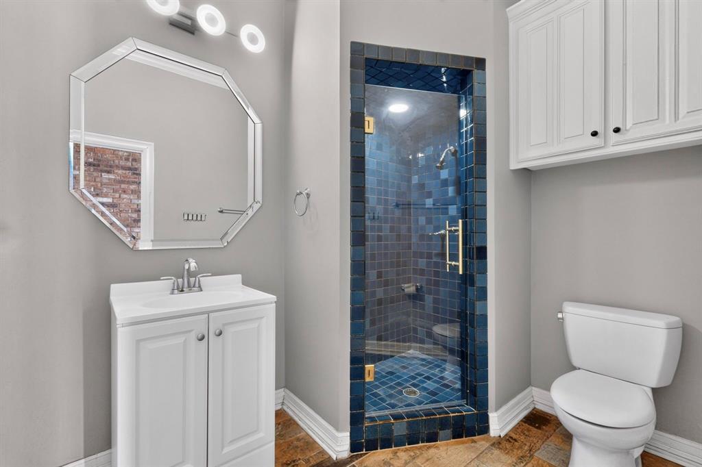 Bathroom featuring a white vanity cabinet, octagonal beveled-edge mirror, wall-mounted cabinetry, and a walk-in tiled shower with a glass door