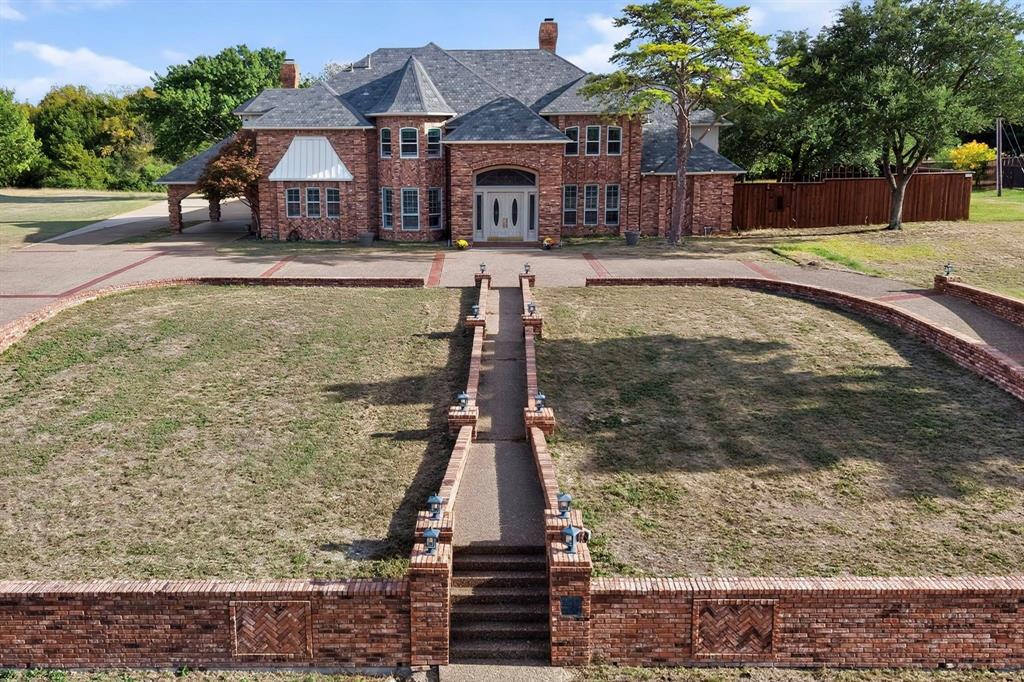 Multi-level brick exterior featuring a multi-gabled roof, a central turret, arched entryway, and a tiered brick perimeter wall with a concrete walkway