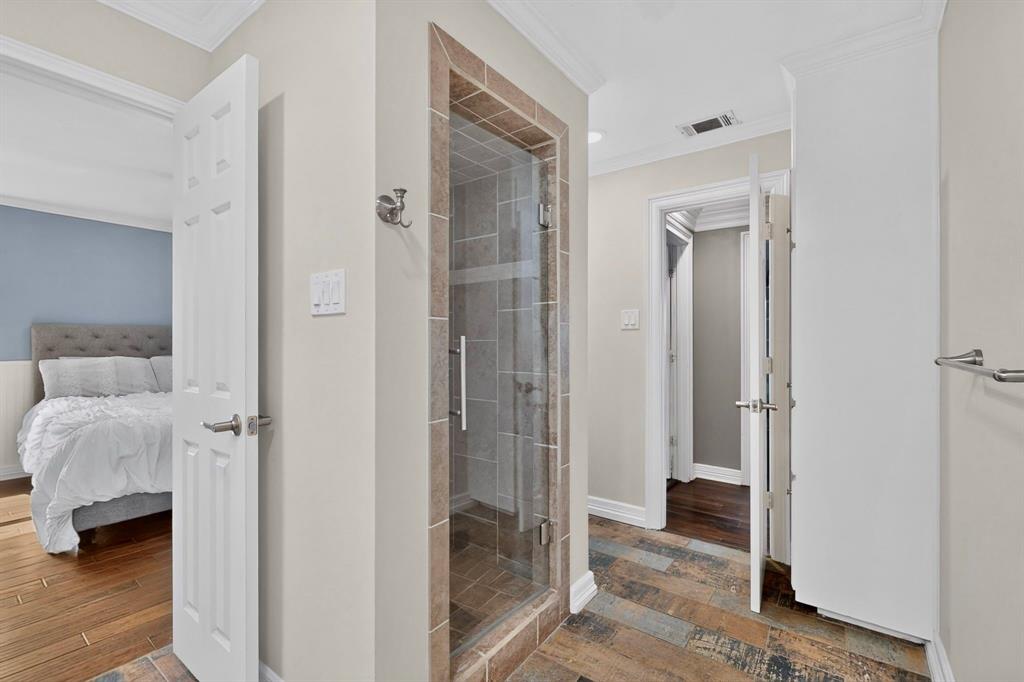Walk-in shower with stone-finish tile surround and glass door, featuring multi-tone tile flooring, crown molding, and built-in floor-to-ceiling cabinetry