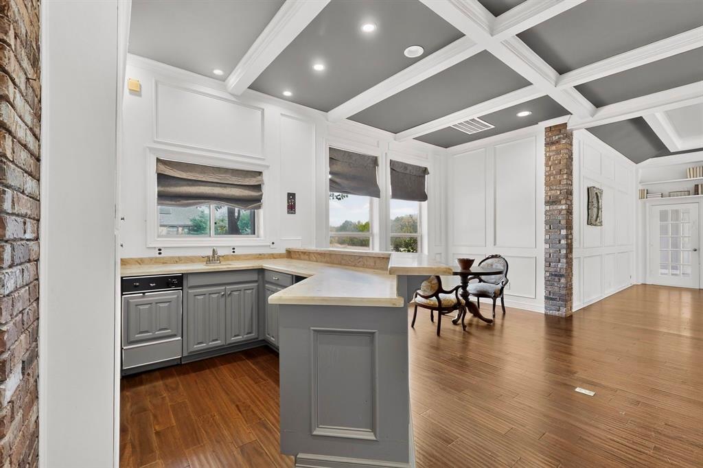 Coffered ceiling with recessed lighting, exposed brick pillars, wainscoting detail, wood-finish flooring, and a stone-topped breakfast bar