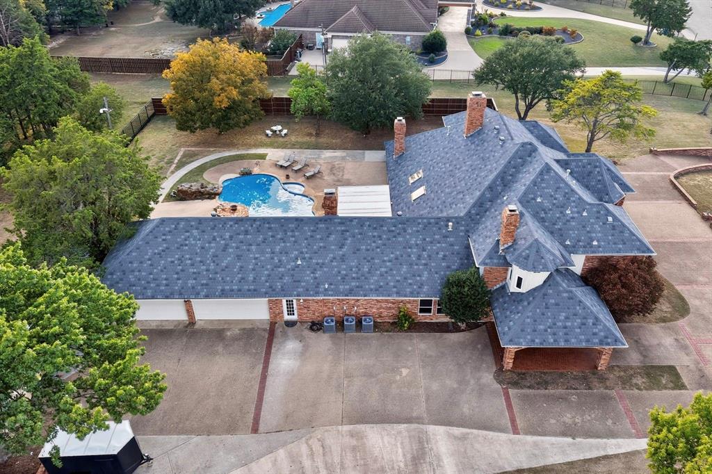 Aerial perspective of a multi-pitched roofline property featuring a brick exterior, in-ground swimming pool, masonry chimneys, and a multi-car garage