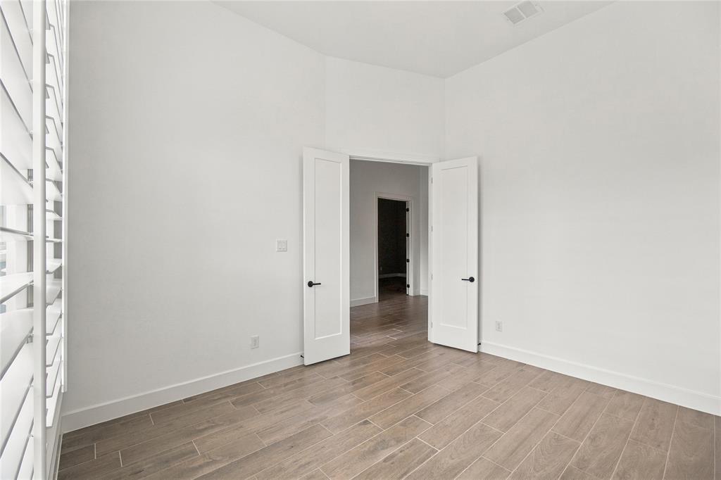 Wood-finish tile flooring, white interior walls, white plantation shutters, and a white interior door with black hardware