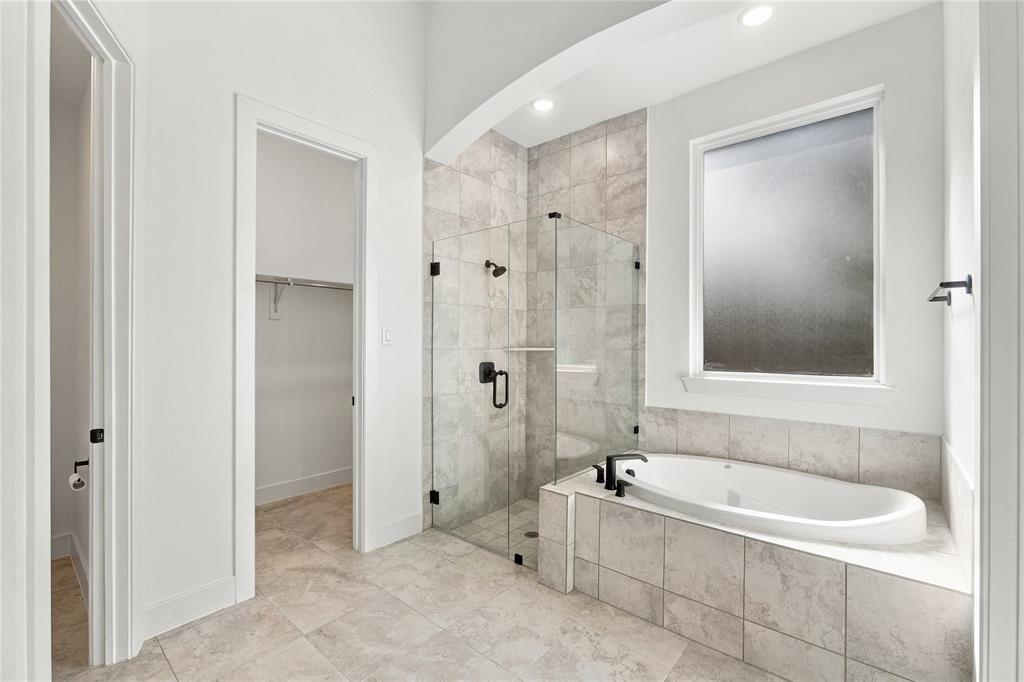 Spacious bathroom featuring a soaking tub, glass-enclosed shower, large privacy window, and tile flooring
