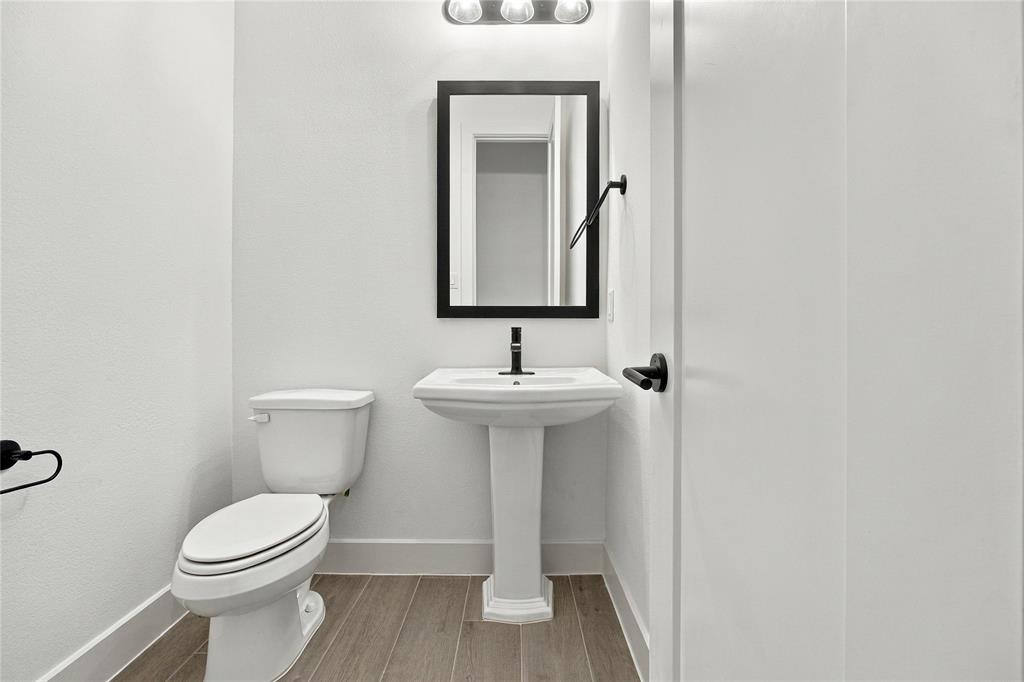 Hallway half-bath features pedestal sink with a rectangular mirror, wood-finish flooring