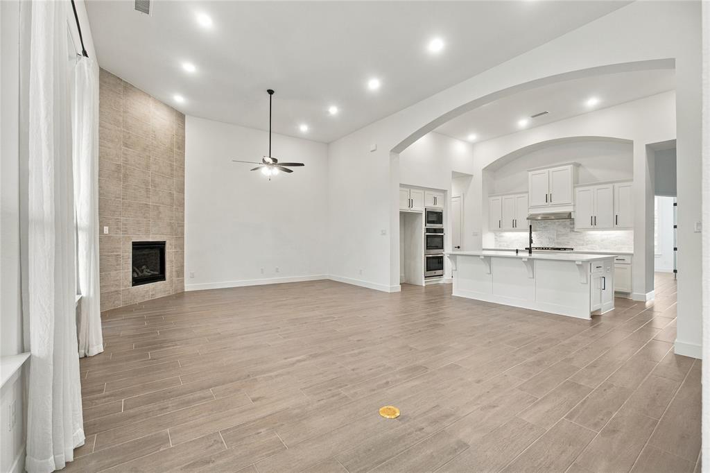 Vaulted ceilings with recessed lighting, floor-to-ceiling tile fireplace, wood-finish flooring, white kitchen cabinetry, and a central kitchen island