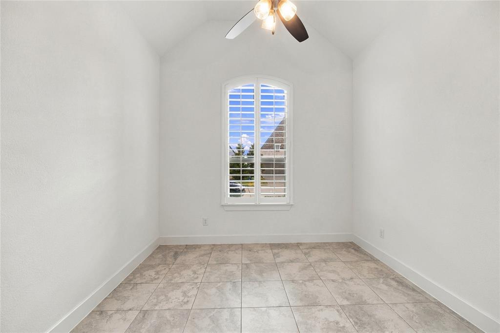 Vaulted ceiling with an attached ceiling fan, arched window with plantation shutters, and large format tile flooring, ensuite bath