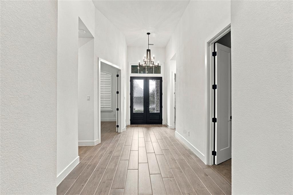 Vaulted entry with wood-look tile flooring, a black double-door entry, a transom window, and a chandelier