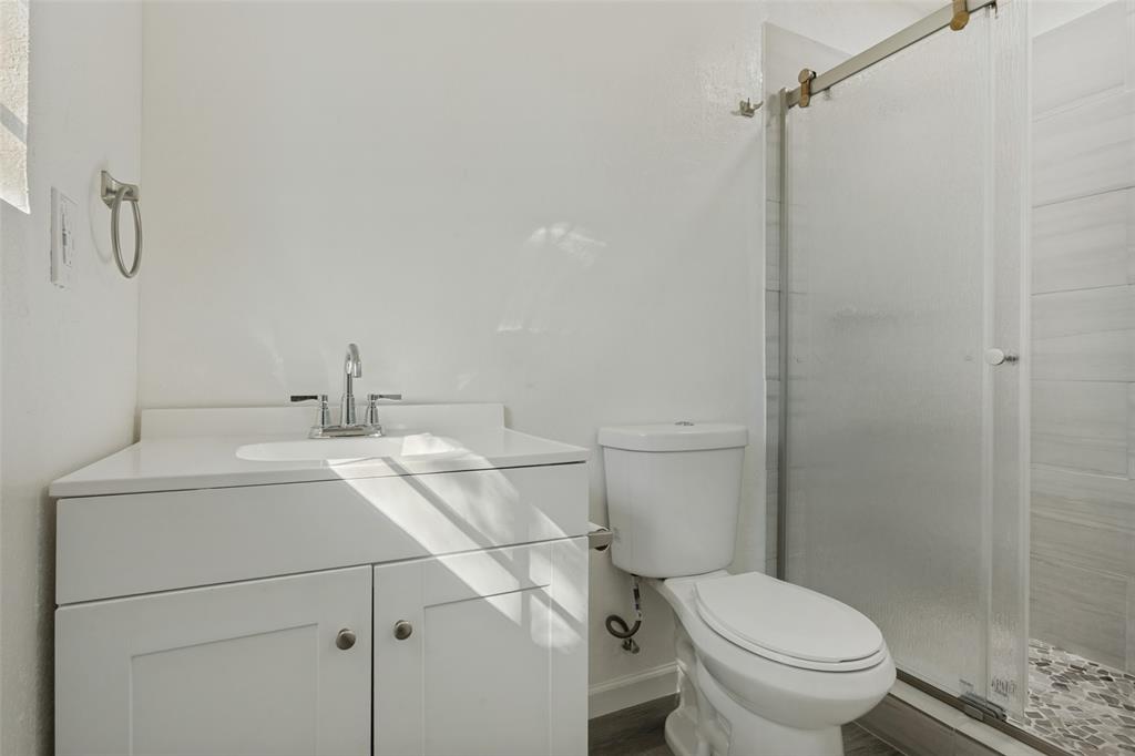 White shaker-style vanity with a solid-surface countertop, under-mount sink, chrome faucet, and walk-in shower with a sliding glass door