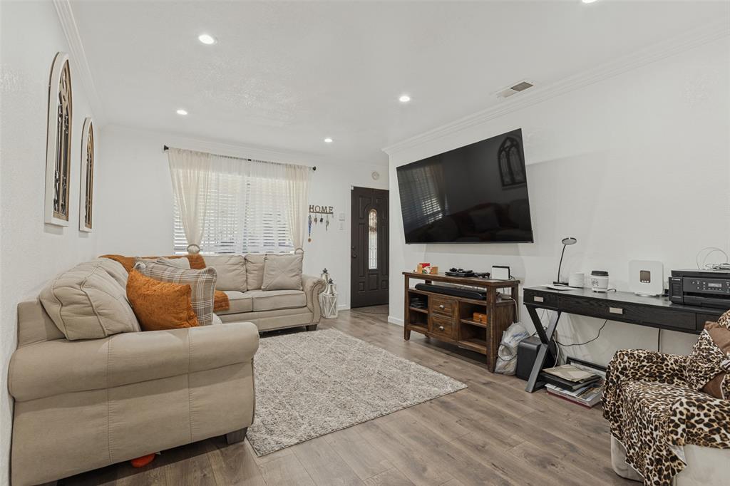 Living area featuring wood-finish flooring, recessed lighting, crown molding, and a paneled entry door