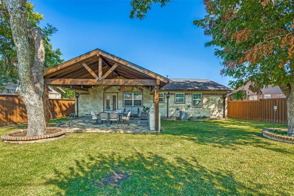 Backyard featuring a stone-clad exterior, covered patio with exposed wood beams, flagstone flooring, and brick-rimmed mature tree planters