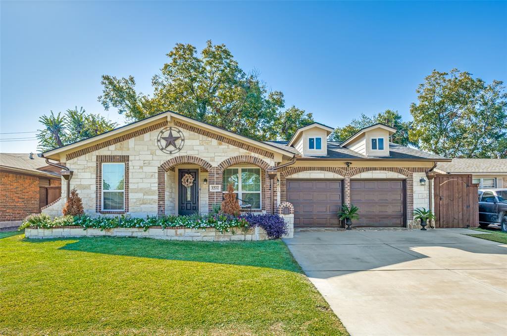 Single-story stone and brick exterior featuring dual arched garage bays, dormer windows, and an elevated stone garden bed