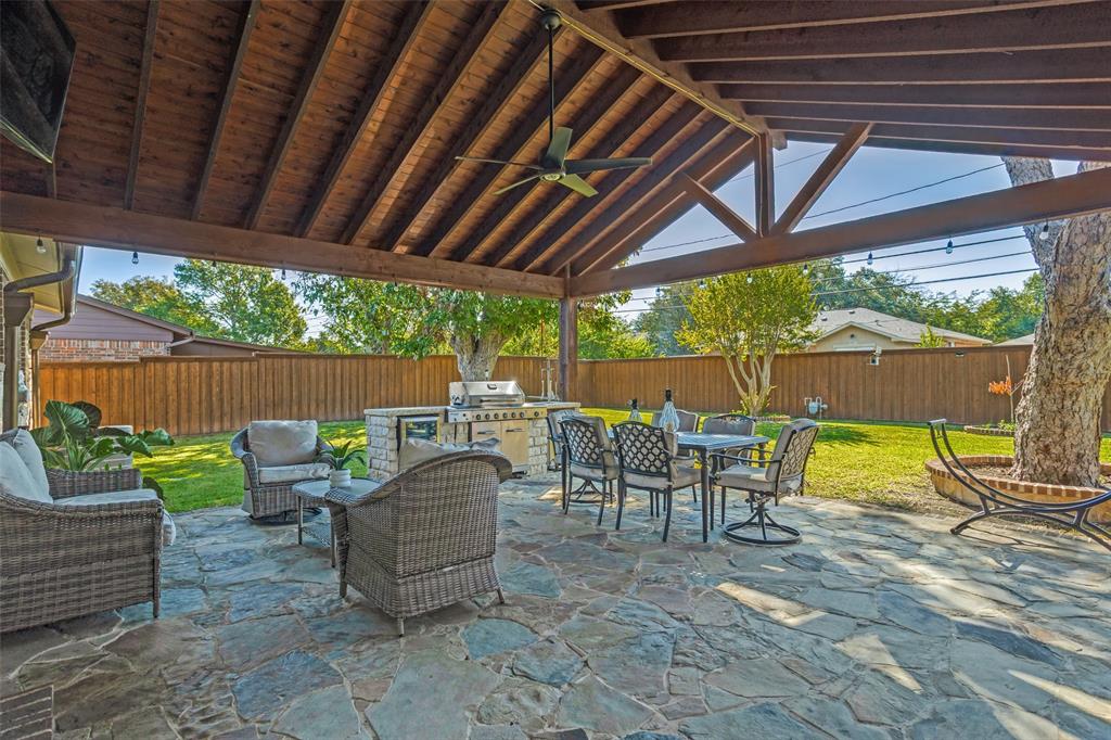 Covered outdoor living space featuring a timber-framed vaulted ceiling, flagstone patio, built-in masonry grill station, and integrated ceiling fan