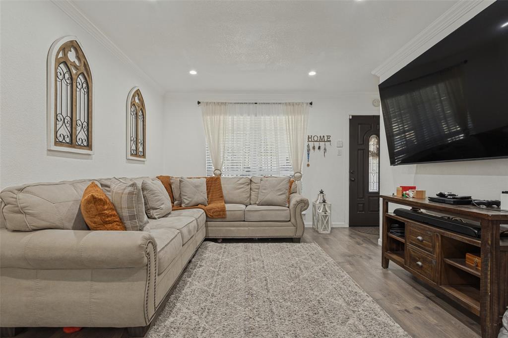 Living space featuring wood-finish flooring, recessed lighting, crown molding, and a dark-toned entry door with decorative glass paneling