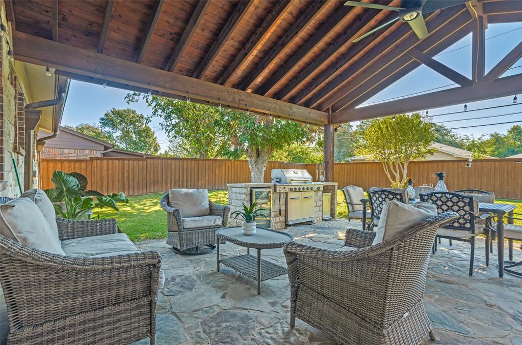Covered patio featuring an exposed timber-beam vaulted ceiling, a built-in outdoor kitchen with stone masonry, a stainless steel grill, and irregular flagstone paving
