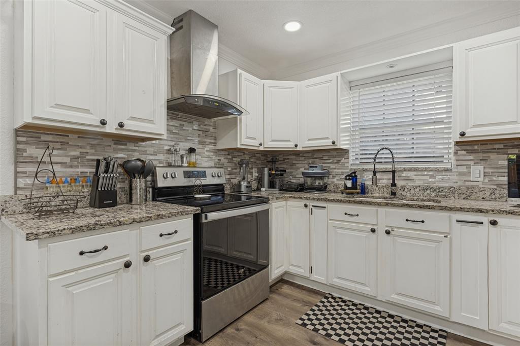 Kitchen featuring white shaker-style cabinetry, stone-finish countertops, linear mosaic tile backsplash, stainless steel range with overhead chimney vent, and wood-finish flooring