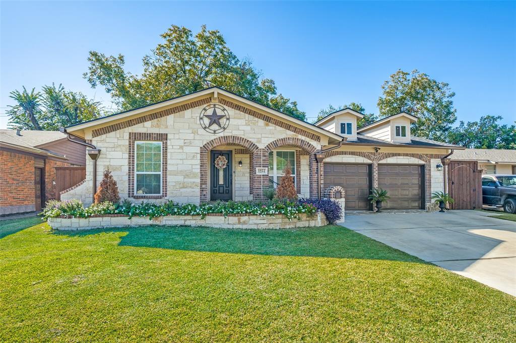 Stone-clad exterior featuring arched brick entryways, two-car garage with wood-finish doors, and a raised stone masonry garden bed