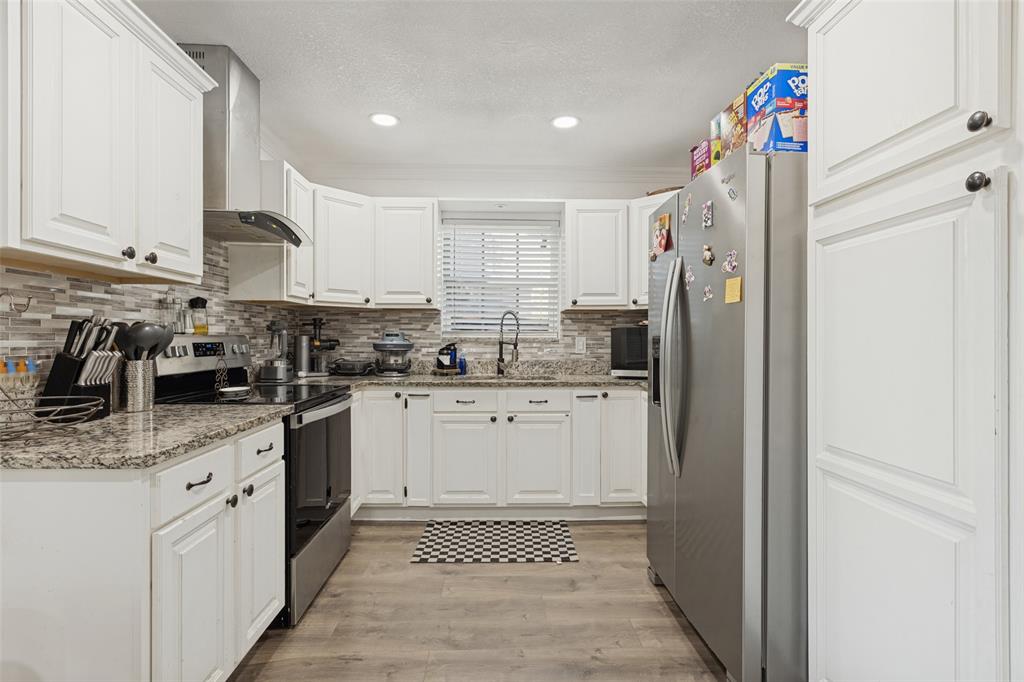 Kitchen featuring white shaker-style cabinetry, stone-finish countertops, stainless steel appliances, a multi-tonal linear tile backsplash, and wood-finish flooring