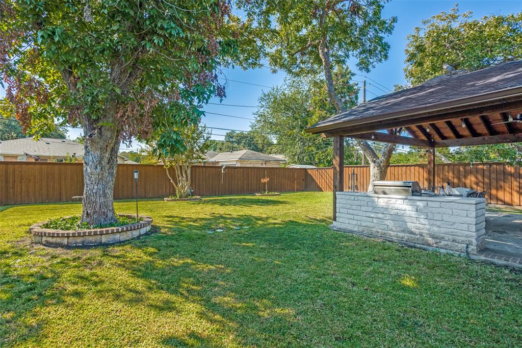 Backyard featuring a covered patio with a built-in masonry grill station, a brick-enclosed tree planter, and perimeter wood fencing